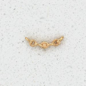 May include: A gold-colored chain link connector with three connected links. The connector is made of a shiny metal and is displayed on a white speckled surface. The chain link is a jewelry component.