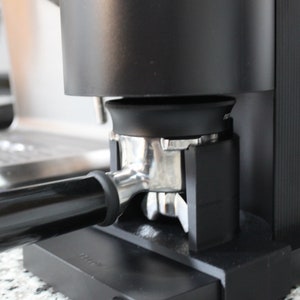 May include: A black espresso machine with a silver portafilter and a black drip tray. The machine has a black and silver design.