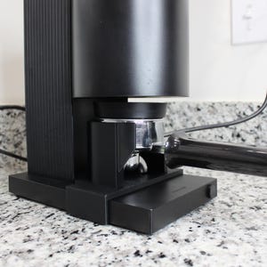 May include: A black espresso machine with a chrome portafilter and a black handle. The machine is sitting on a countertop.