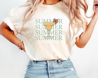 May include: A white t-shirt with a green and yellow graphic of a margarita glass with a strawberry on the rim. The text "SUMMER" is repeated four times in green.