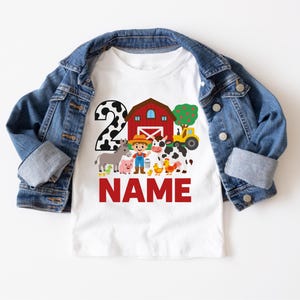 May include: White t-shirt with a red barn, a cow, a pig, a donkey, a rooster, a tractor, and a farmer. The number 2 is in the background with black and white spots. The text "NAME" is in red letters below the farm scene.