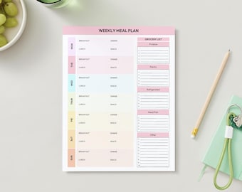 Op de afbeelding: Een pastelkleurig wekelijks maaltijdplan-notitieblok met secties voor elke dag van de week, inclusief ontbijt, lunch, diner en snack. Er is ook een boodschappenlijst opgenomen. Een potlood en een klein notitieboekje met sleutelhanger.