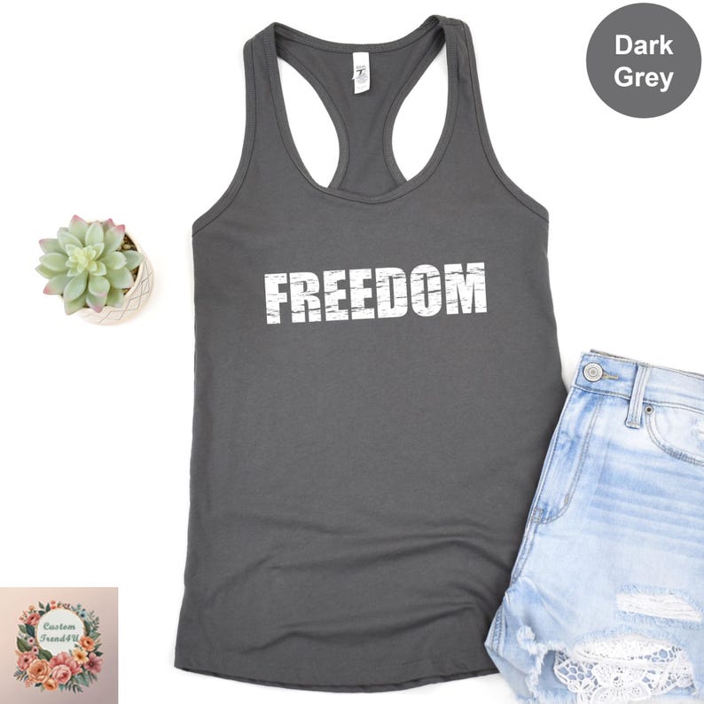 a grey tank top with the word "FREEDOM" printed on it, along with a pair of denim shorts and a small potted succulent plant.
