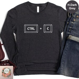 May include: Dark grey long-sleeve shirt with the white text "CTRL + C" printed on the front. The design features the keyboard keys for copy and paste. The shirt is made of a soft material.