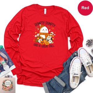 a red long-sleeved t-shirt with a cartoon character and text, along with a pair of jeans and white sneakers, all laid out on a white background.