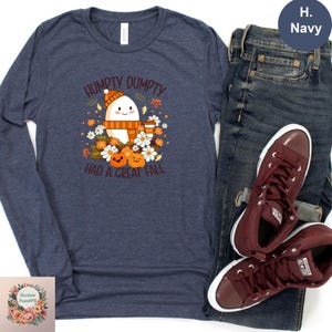 a navy blue long-sleeved t-shirt with a graphic design, a pair of dark blue jeans, and a pair of burgundy sneakers, all laid out on a white background.