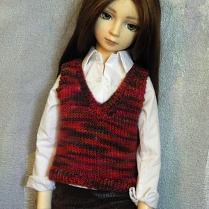 May include: A doll wearing a white shirt with a red and brown striped waistcoat and a brown skirt.