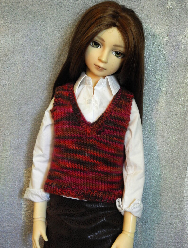 May include: A doll wearing a white shirt with a red and brown striped waistcoat and a brown skirt.