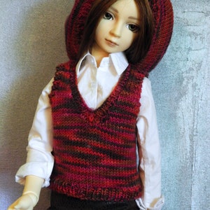 May include: A doll wearing a red and brown striped knitted waistcoat, a white button-down shirt, and a red knitted hat.