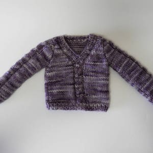 Puede incluir: Un c&aacute;rdigan de punto a rayas morado y blanco con cuello en V y cierre de botones.