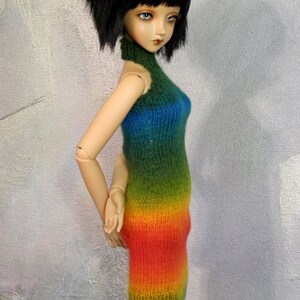 May include: A doll wearing a rainbow ombre knitted dress with a high neck.