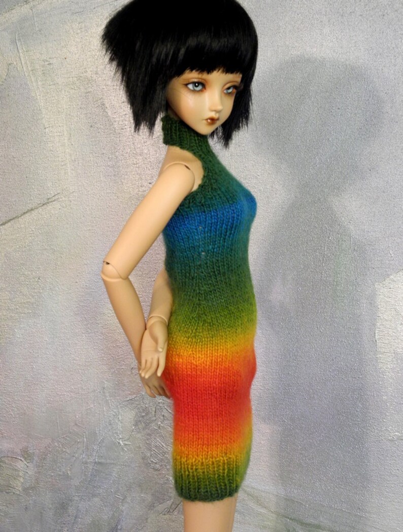 May include: A doll wearing a rainbow ombre knitted dress with a high neck.