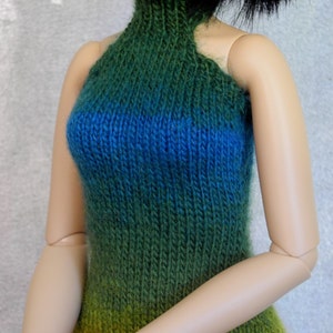 May include: A doll wearing a green, blue, and orange ombre knitted halter top.