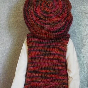 May include: A knitted waistcoat with brown, red and black stripes. The waistcoat is worn over a white shirt and a brown and red knitted hat.