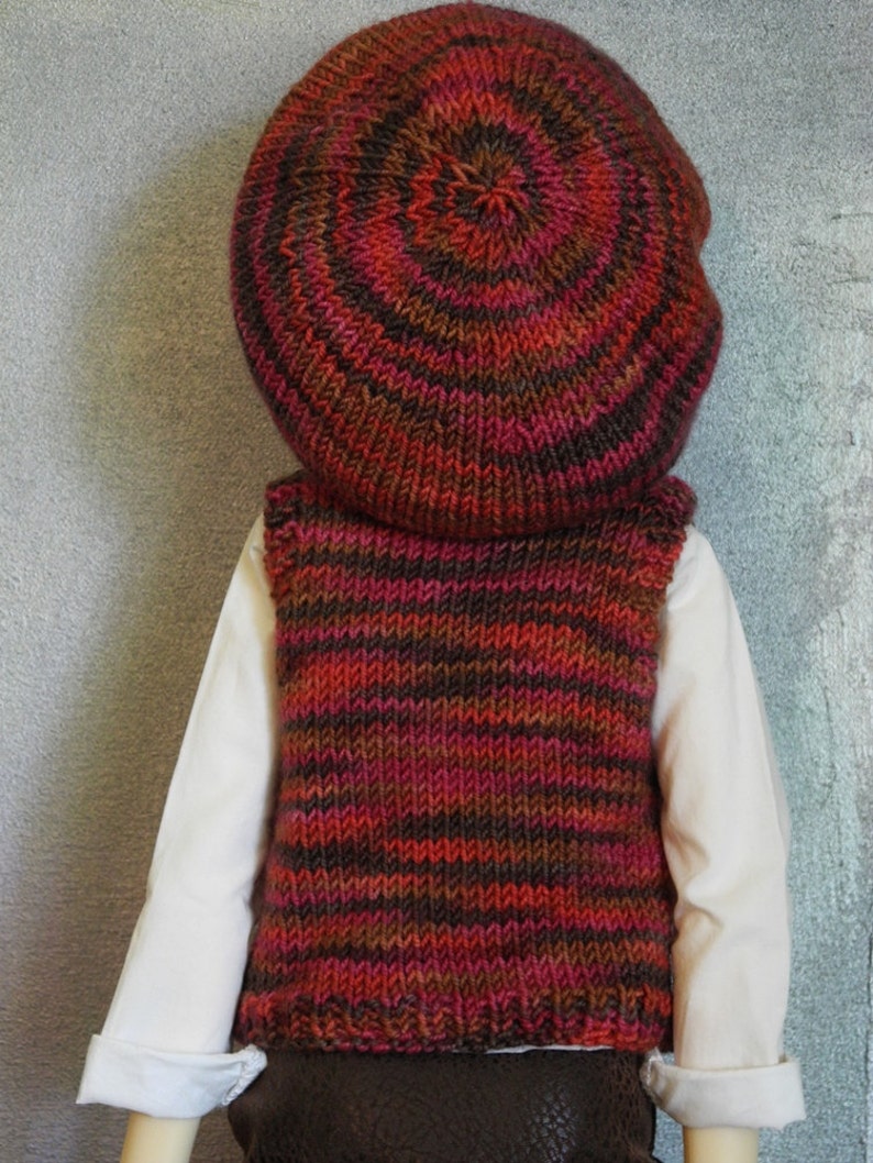 May include: A knitted waistcoat with brown, red and black stripes. The waistcoat is worn over a white shirt and a brown and red knitted hat.