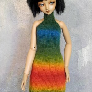 May include: A doll wearing a rainbow knit halter dress. The dress is green, blue, yellow, orange, and red.