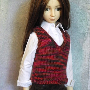 May include: A doll wearing a white shirt with a brown and red striped waistcoat and a brown skirt.