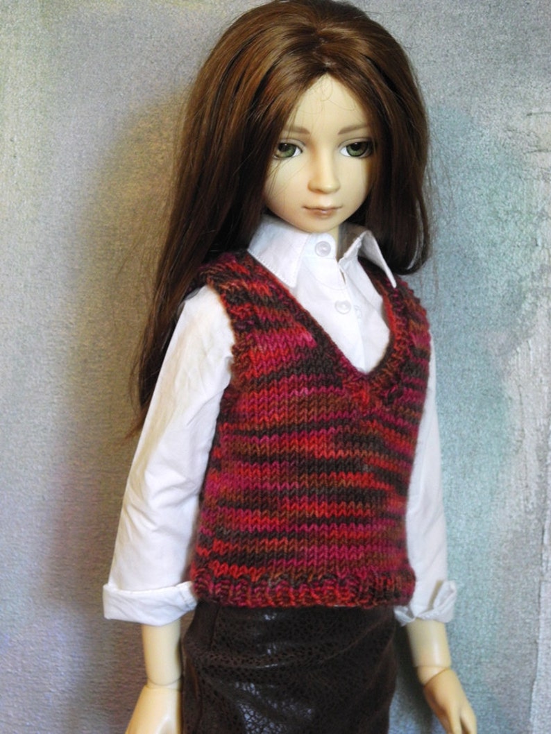 May include: A doll wearing a white shirt with a brown and red striped waistcoat and a brown skirt.