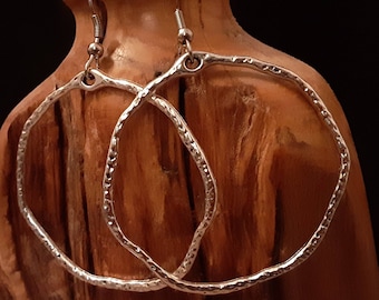 May include: A pair of silver hoop earrings with a hammered texture. The earrings are hanging from a wooden surface.