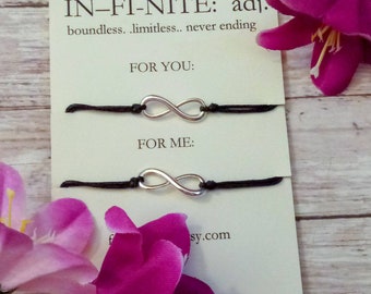 May include: Two black string bracelets with silver infinity symbol charms. The bracelets are packaged on a card with the text "IN-FI-NITE: adj. boundless. limitless. never ending FOR YOU: FOR ME: sy.com"