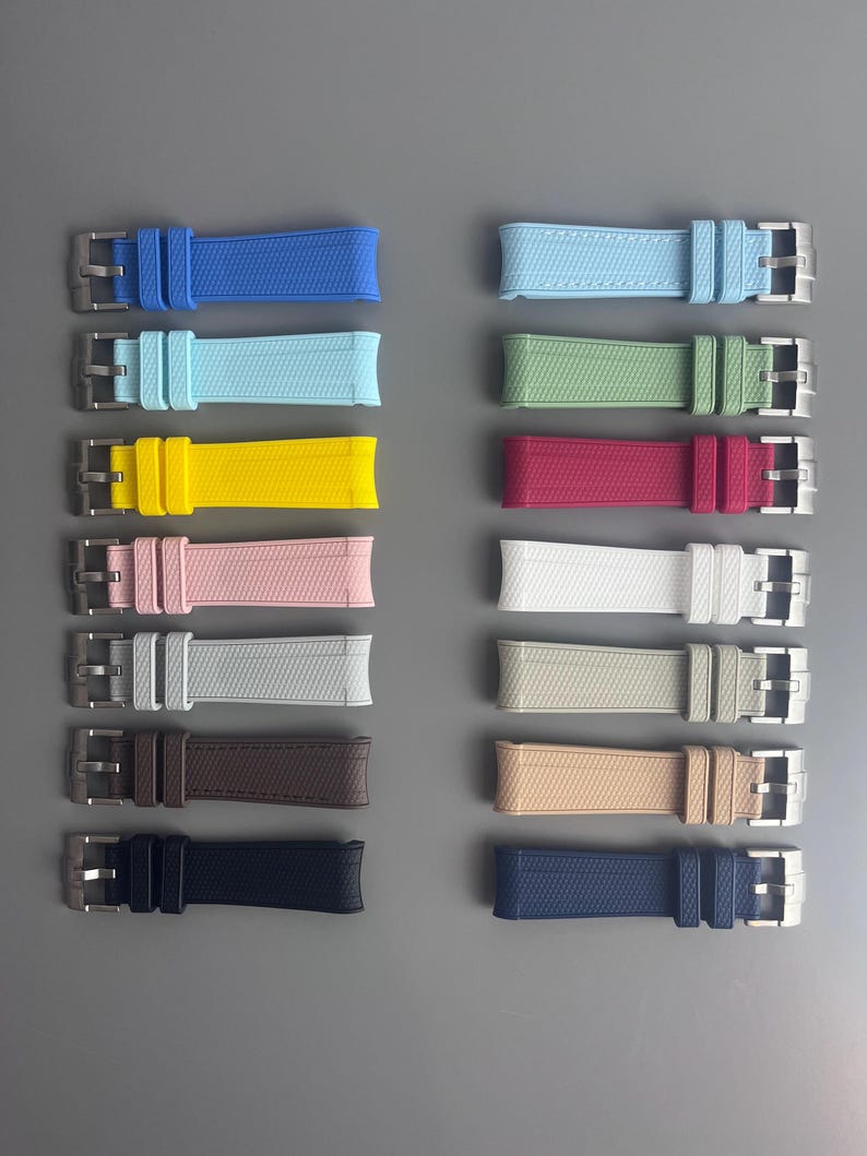 Op de afbeelding: Een set van 10 verschillende gekleurde horlogebandjes. De bandjes zijn gemaakt van een getextureerd rubber materiaal en hebben een zilveren gesp. De kleuren omvatten blauw, lichtblauw, geel, roze, wit, lichtgrijs, bruin, beige, donkerblauw en zwart.