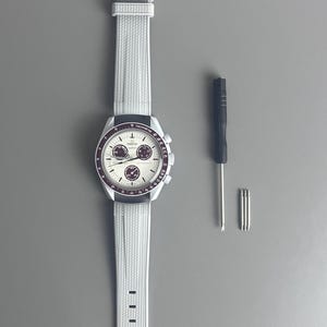 Op de afbeelding: Een wit horloge met een zilveren wijzerplaat en een wit rubberen band. Het horloge heeft drie subwijzerplaten en een tachymeterschaal. Het horloge wordt geleverd met een kleine schroevendraaier en drie kleine schroeven.