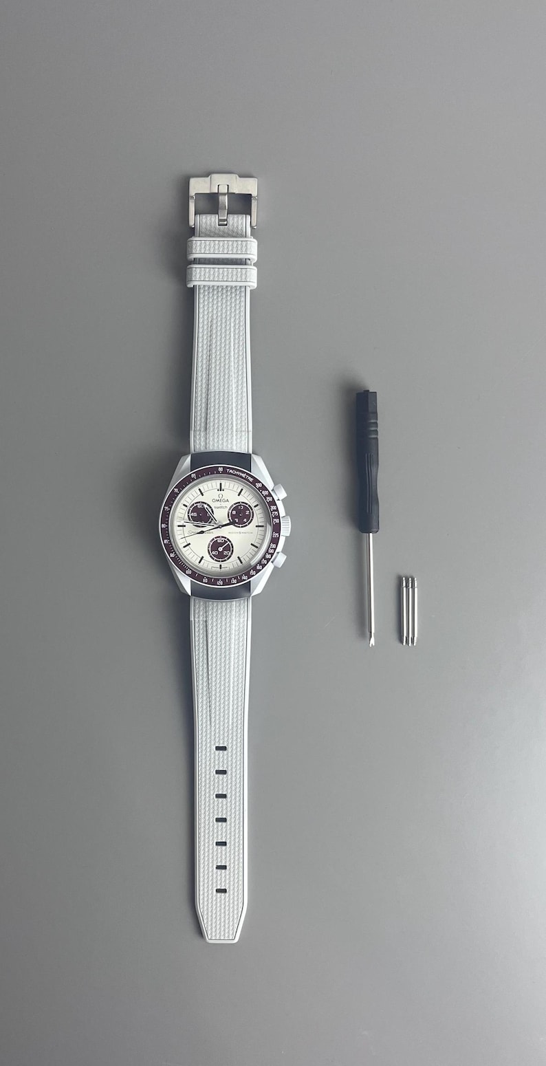 Op de afbeelding: Een wit horloge met een zilveren wijzerplaat en een wit rubberen band. Het horloge heeft drie subwijzerplaten en een tachymeterschaal. Het horloge wordt geleverd met een kleine schroevendraaier en drie kleine schroeven.