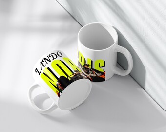 May include: Two white ceramic mugs with black and yellow text and a race car design. One mug displays the name "LANDO" in black and yellow, while the other says "NORRIS Chrome". The mugs are on a white surface.