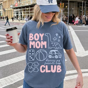 Blue Jean Comfort Colors boy mom club shirt featuring dinosaur toy car puzzle ball illustrations raising my favorite boys slogan garment dyed relaxed motherhood tee thoughtful mothers day gift ships without price tag