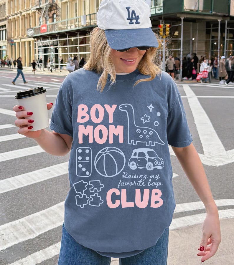 Blue Jean Comfort Colors boy mom club shirt featuring dinosaur toy car puzzle ball illustrations raising my favorite boys slogan garment dyed relaxed motherhood tee thoughtful mothers day gift ships without price tag