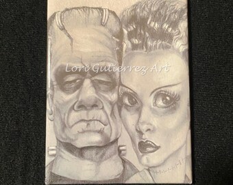 Peut inclure: Dessin en noir et blanc de Frankenstein et de sa fiancée. Le dessin est sur fond blanc et porte la signature de l'artiste "Lori Gutierrez Art".