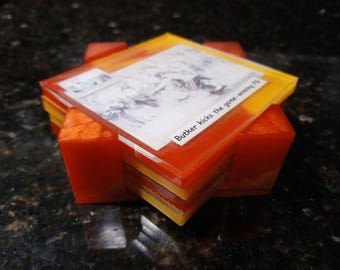 Könnte beinhalten: Ein Satz quadratischer Untersetzer aus Harz in Orange- und Gelbtönen. Jeder Untersetzer zeigt ein gedrucktes Bild mit dem Text "Butker kicks the game-winning FG". Die Untersetzer sind auf einem passenden Halter aus orangefarbenem Harz gestapelt.