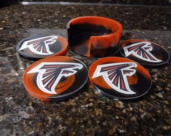 Puede incluir: Juego de cuatro posavasos redondos y un soporte. Cada posavasos presenta el logotipo de los Atlanta Falcons en blanco, rojo y negro. Los posavasos y el soporte tienen un acabado brillante con detalles en naranja y negro.