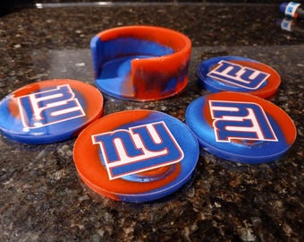 May include: A set of five resin coasters and a holder. The coasters are round, with a blue and red swirl design and the letters "NY" in white. The holder is a matching blue and red colour.