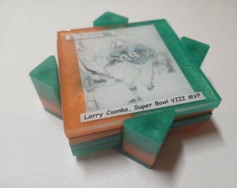 Puede incluir: Un posavasos de resina hecho a mano con una imagen en blanco y negro de un jugador de fútbol americano. El posavasos tiene detalles en naranja y verde, con el texto "Larry Csonka, Super Bowl VIII MVP".