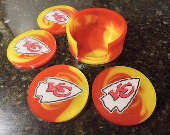 Könnte beinhalten: Satz mit vier roten und gelben Untersetzern mit einem weißen Kansas City Chiefs Logo. Die Untersetzer werden mit einem passenden roten und gelben Halter geliefert.
