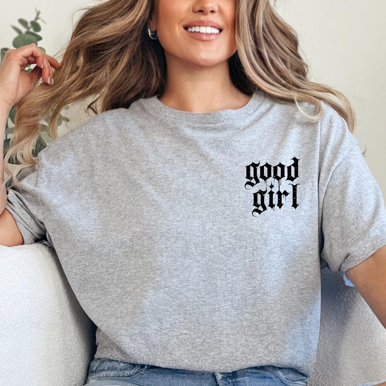 a woman sitting on a couch wearing a grey t - shirt with the words good