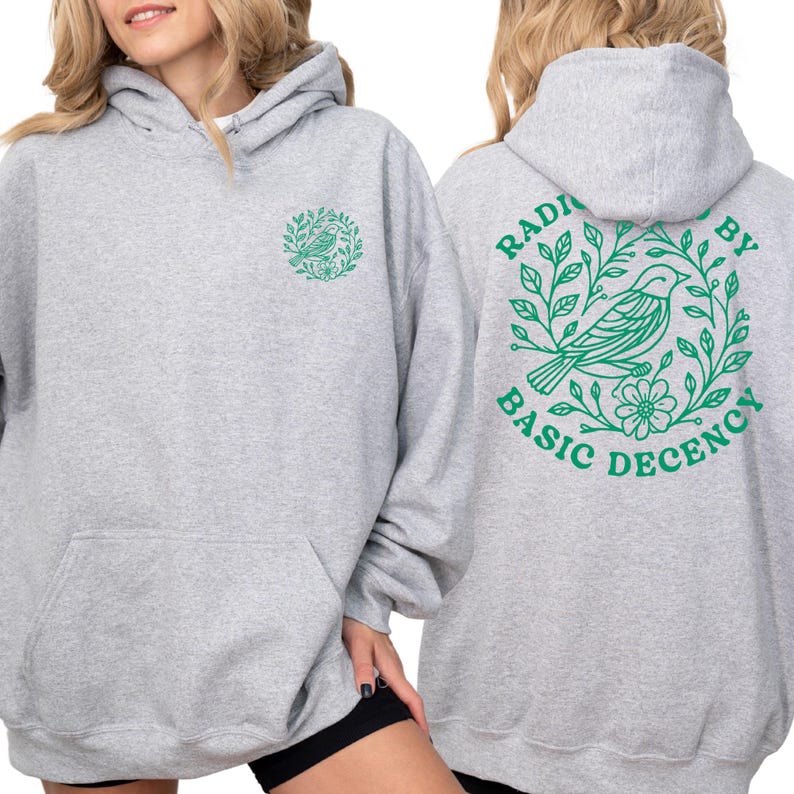 A woman wearing a grey hooded sweatshirt with a green graphic design on the back.