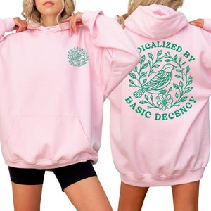 A woman wearing a pink hoodie with a green design on the back.