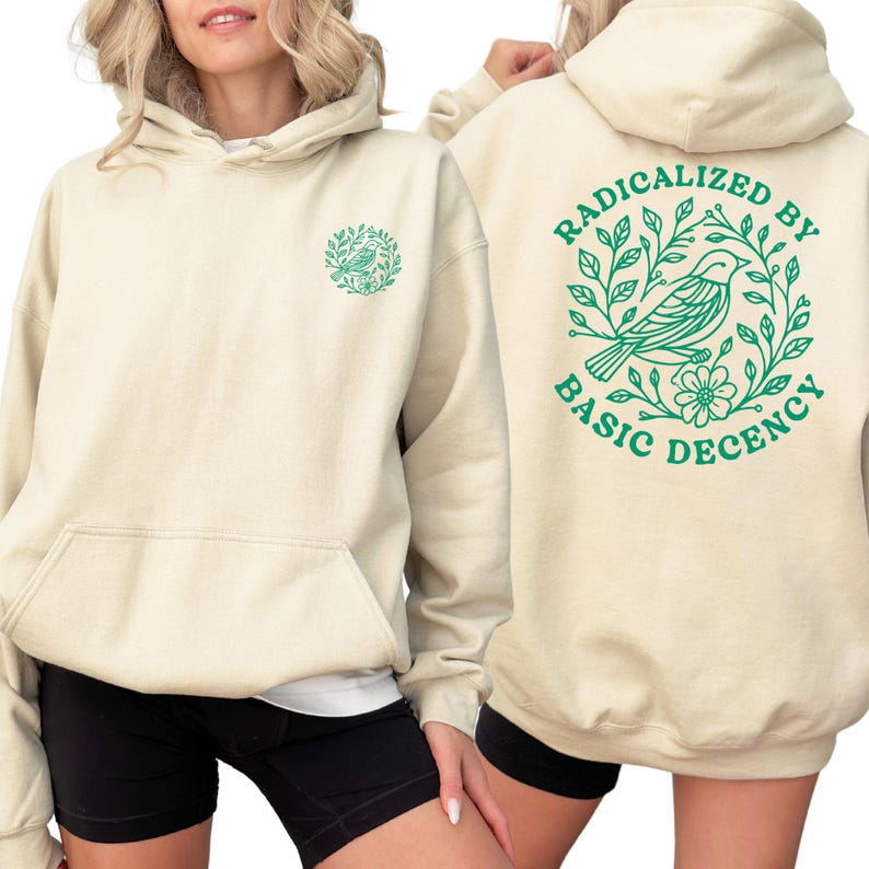 A woman wearing a cream-colored hoodie with a green graphic design on the back.