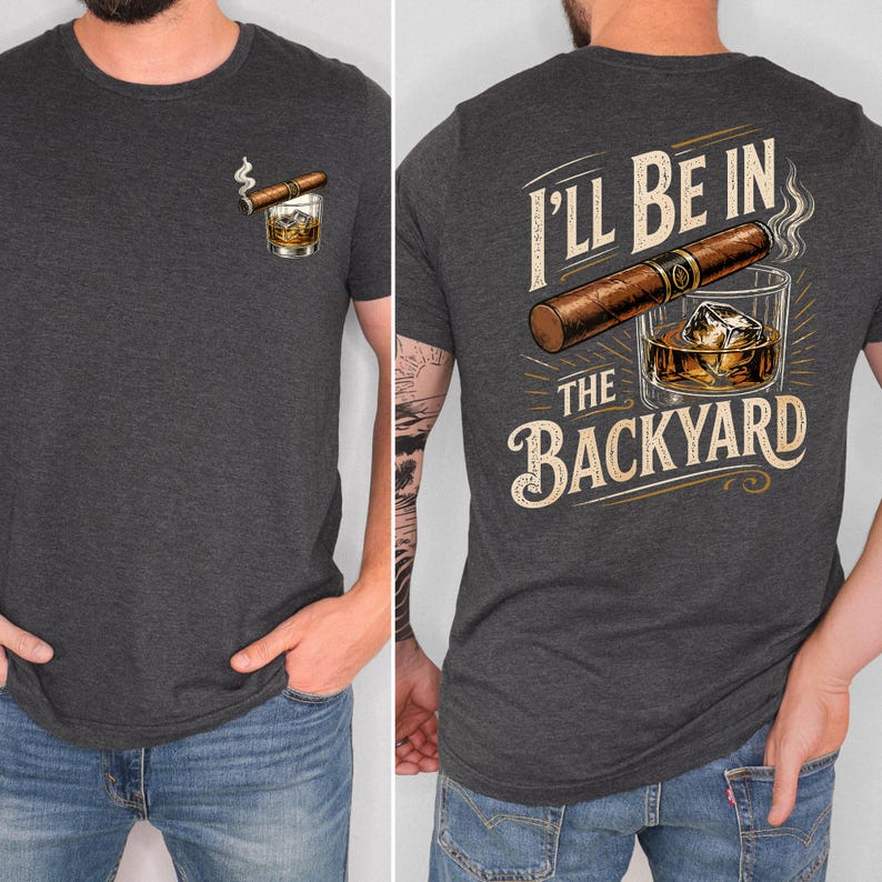 May include: A dark charcoal gray t-shirt featuring a small graphic on the front left chest of a cigar resting on a glass of whiskey with ice. The back of the shirt displays a large cigar, a glass of whiskey with ice, and the text I'LL BE IN THE BACKYARD.