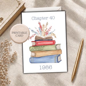 May include: A white greeting card featuring a watercolor illustration of a stack of four books in red, green, tan, and blue. An open book sits on top with colorful wildflowers emerging from the pages. The text reads Chapter 40 at the top and 1986 below.