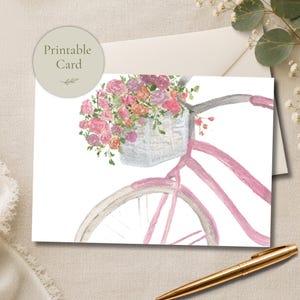 以下が含まれることがあります： ピンクの自転車と、ピンク、オレンジ、紫の花で溢れる白いバスケットの水彩画が描かれた印刷可能なカード。カードの左上隅には「Printable Card」という文字が書かれた円形のラベルが付いています。