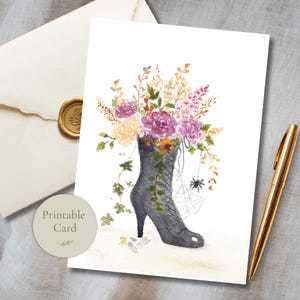 Pode incluir: Um cartão imprimível com uma ilustração em aguarela de uma bota preta com atacadores que serve de vaso para um ramo de flores roxas e amarelas, hera verde e uma pequena aranha com uma teia. O cartão está ao lado de uma caneta dourada.