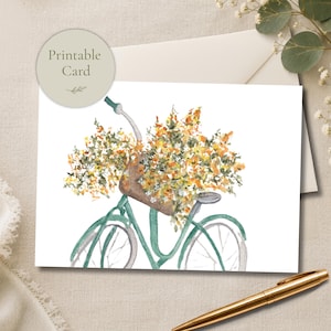 Può includere: Una carta stampabile con un'illustrazione ad acquerello di una bicicletta verde con un cestino marrone pieno di fiori gialli e arancioni. Il testo Printable Card è visualizzato in un badge circolare nell'angolo in alto a sinistra.
