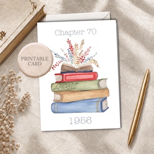 May include: A white greeting card featuring a watercolor illustration of a stack of four books with an open book on top, topped with colorful wildflowers. The text reads Chapter 70 at the top and 1956 at the bottom in a dark blue font.