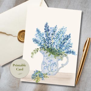 Può includere: Un biglietto d'auguri con un'illustrazione ad acquerello di fiori blu in una brocca di ceramica decorata. Il biglietto riporta il testo Printable Card. Una penna dorata e una busta color crema con un sigillo di cera dorato sono vicine.