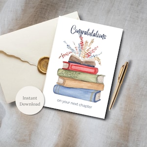 May include: A white greeting card with the word "Congratulations" in navy script, featuring a stack of books topped with flowers. The text "on your next chapter" is below the books. An envelope with a gold seal and a gold pen are also present.