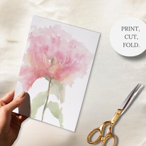 A hand holding a hand-painted card featuring a watercolor peony, gold scissors and a badge with the wording Print, Cut, Fold
