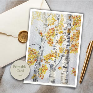 May include: A rectangular greeting card featuring a watercolor painting of three birch trees with white bark and vibrant yellow and orange autumn leaves against a light gray background. The card is positioned next to a gold pen and an envelope.